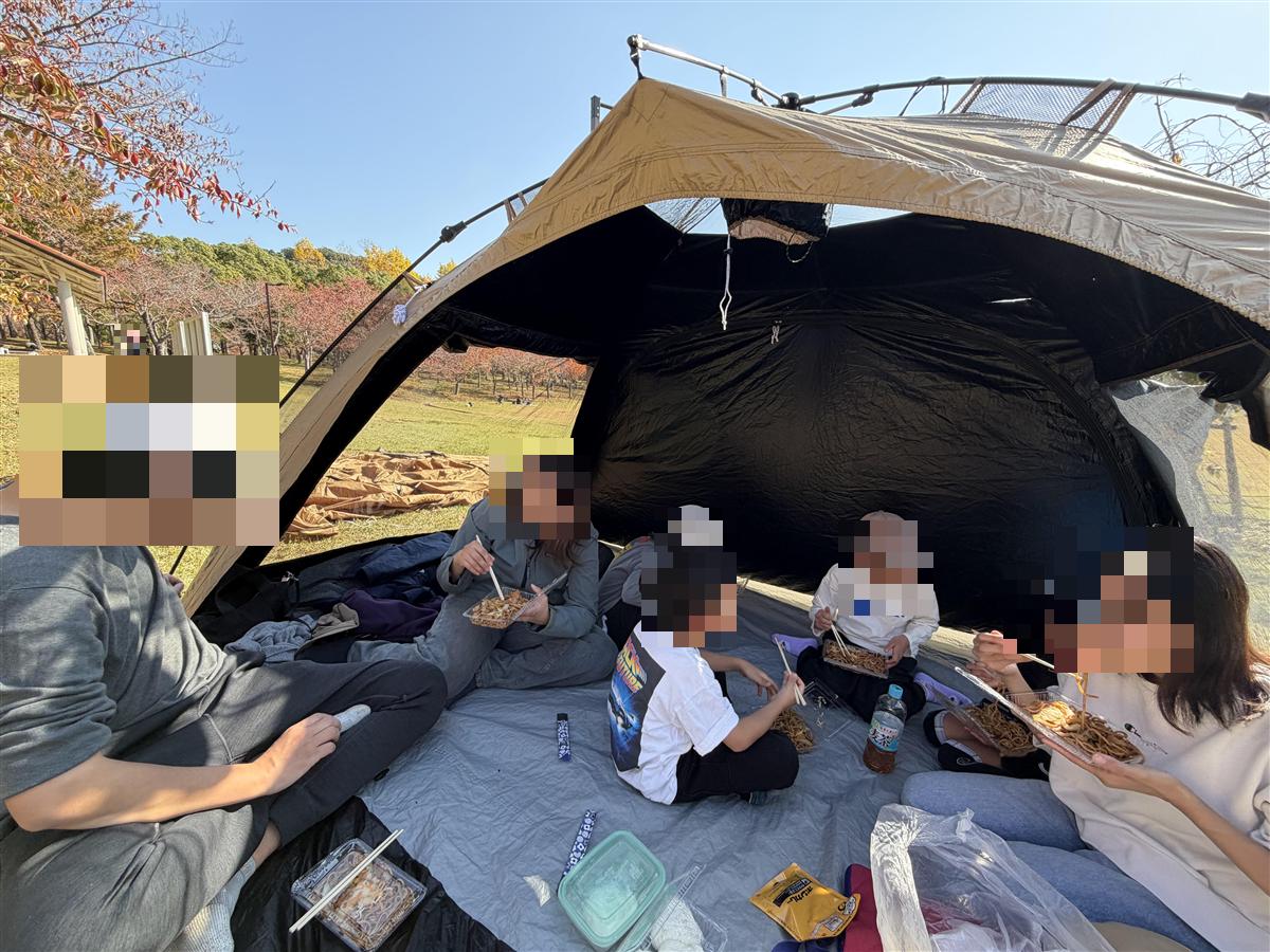わがやのシェードの中で、大人と子ども7人がお昼ごはんを食べている様子。出入り口を全開にして下のシートも使っている